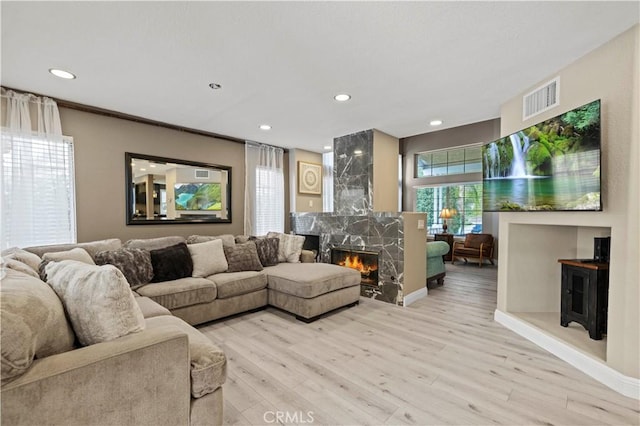 living area with light wood finished floors, recessed lighting, visible vents, and a high end fireplace