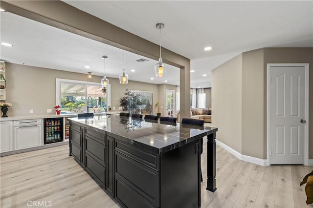 kitchen with light wood-style flooring, beverage cooler, dark cabinetry, plenty of natural light, and a kitchen bar