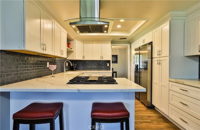 kitchen featuring island range hood, a peninsula, a sink, gas stovetop, and stainless steel fridge with ice dispenser