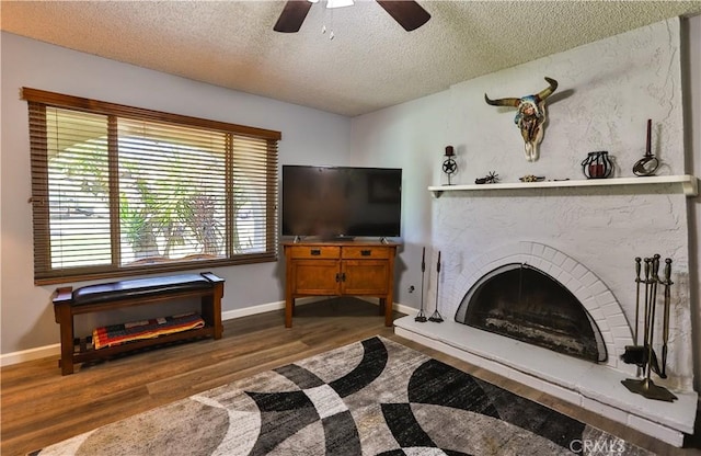 living room with baseboards, a fireplace with raised hearth, ceiling fan, wood finished floors, and a textured ceiling