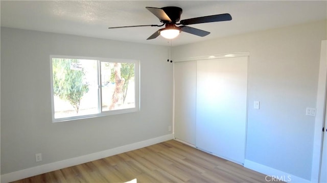 unfurnished bedroom featuring light wood-type flooring, a ceiling fan, baseboards, and a closet