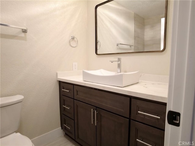 bathroom with toilet, baseboards, and vanity