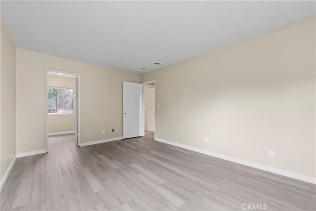 empty room featuring light wood finished floors, visible vents, and baseboards