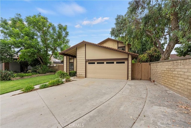 view of front facade with concrete driveway, a tile roof, an attached garage, fence, and a front yard