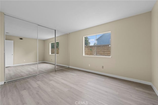 unfurnished bedroom featuring a closet, visible vents, baseboards, and wood finished floors