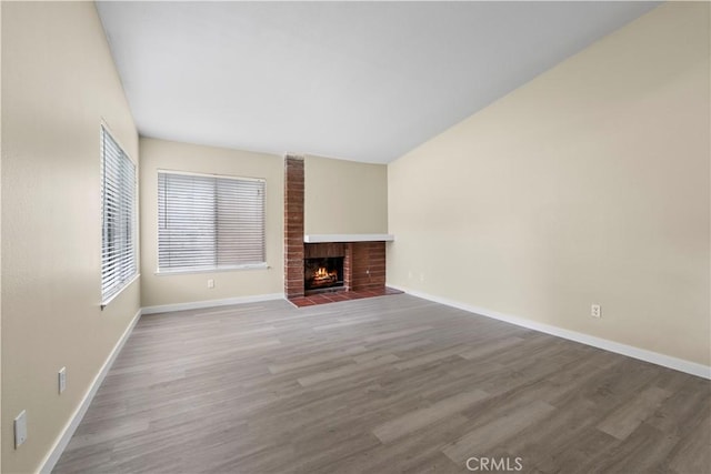 unfurnished living room featuring a brick fireplace, baseboards, and wood finished floors