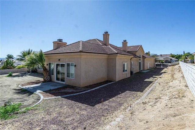 view of property exterior featuring a tile roof, a chimney, fence, a patio area, and stucco siding