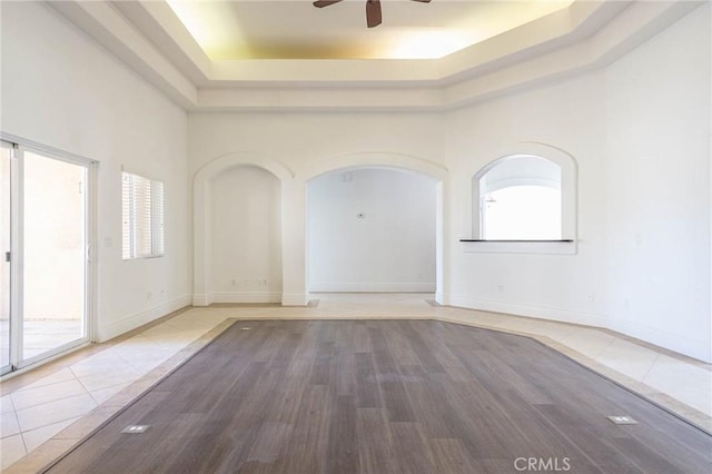 tiled empty room featuring a high ceiling, a tray ceiling, and a wealth of natural light