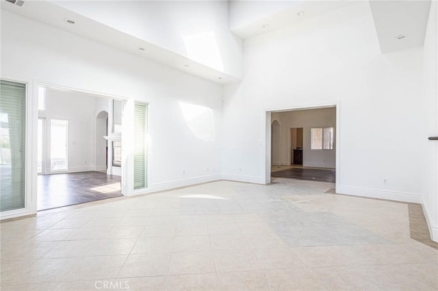 empty room featuring arched walkways, a high ceiling, baseboards, and light tile patterned floors