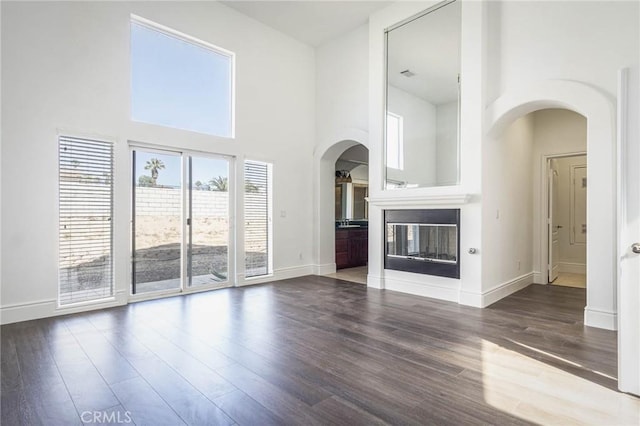 unfurnished living room with arched walkways, a glass covered fireplace, wood finished floors, and a towering ceiling