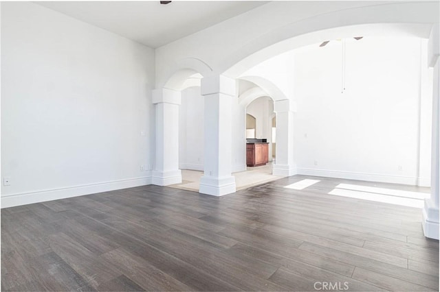 unfurnished room featuring arched walkways, ceiling fan, wood finished floors, and baseboards