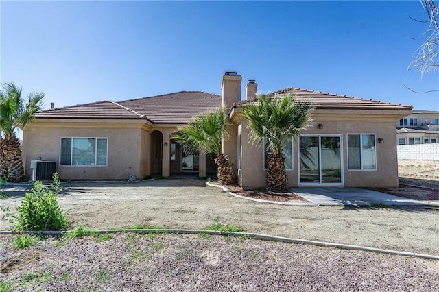 rear view of property featuring a patio, cooling unit, driveway, stucco siding, and a chimney