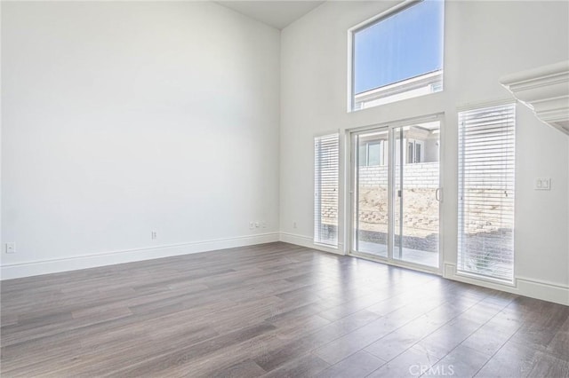 unfurnished room with a towering ceiling, baseboards, and wood finished floors