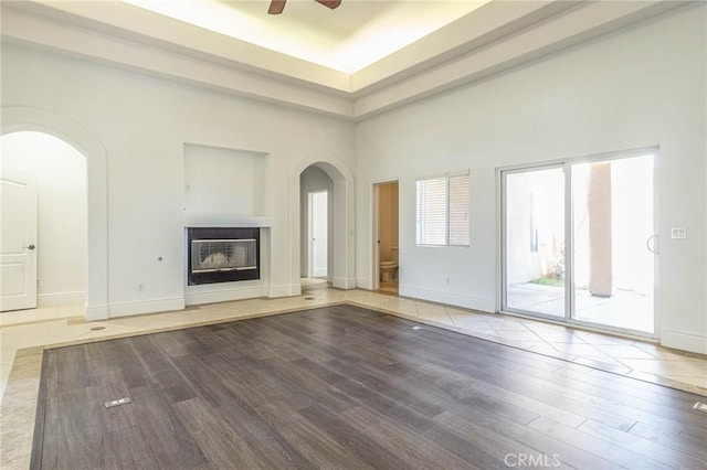 unfurnished living room with arched walkways, ceiling fan, and wood finished floors