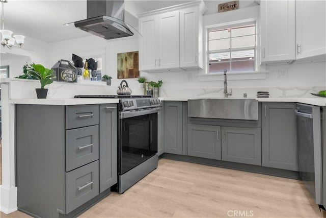 kitchen with appliances with stainless steel finishes, gray cabinets, and wall chimney range hood