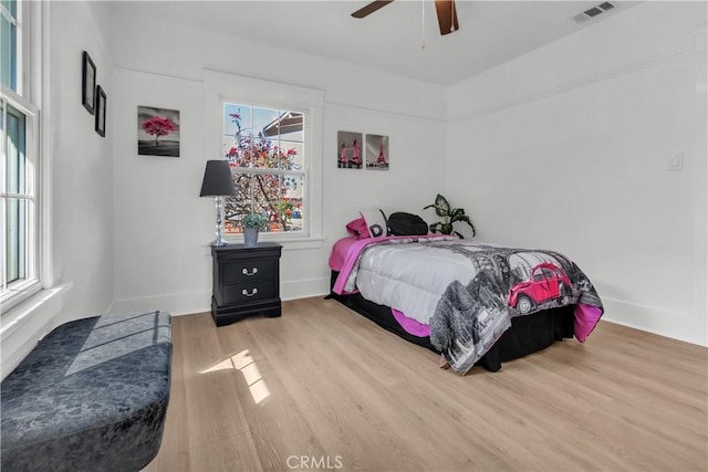 bedroom with ceiling fan, visible vents, baseboards, and wood finished floors