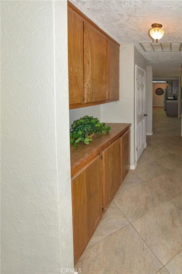 hall with light tile patterned floors, a textured ceiling, visible vents, and attic access