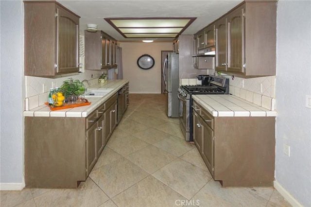 kitchen with tile counters, decorative backsplash, appliances with stainless steel finishes, a sink, and under cabinet range hood