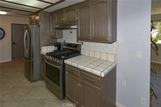 kitchen featuring tasteful backsplash, tile counters, appliances with stainless steel finishes, under cabinet range hood, and light tile patterned flooring