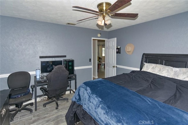 bedroom featuring a ceiling fan, visible vents, a textured wall, and wood finished floors