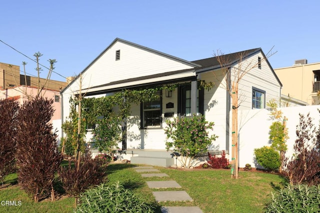 bungalow-style home with covered porch, fence, and a front lawn