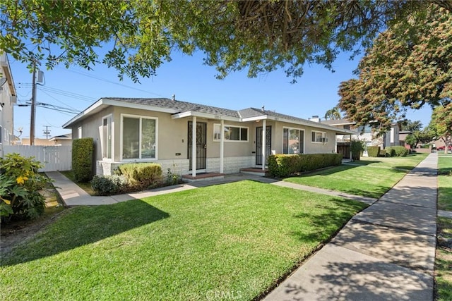 view of front of house with a front yard, stone siding, fence, and stucco siding