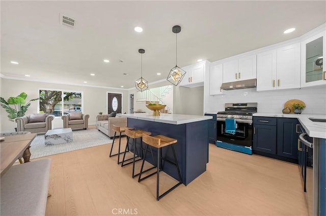 kitchen with a breakfast bar area, under cabinet range hood, white cabinets, open floor plan, and stainless steel gas range