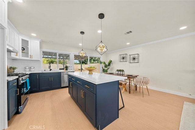 kitchen with light countertops, appliances with stainless steel finishes, white cabinets, a sink, and light wood-type flooring