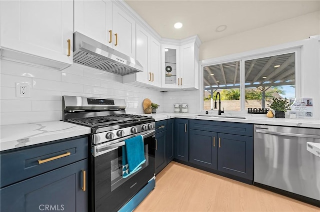 kitchen with stainless steel appliances, white cabinetry, a sink, blue cabinets, and under cabinet range hood