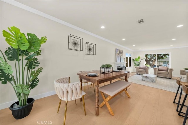 dining room with light wood finished floors, baseboards, visible vents, ornamental molding, and a fireplace