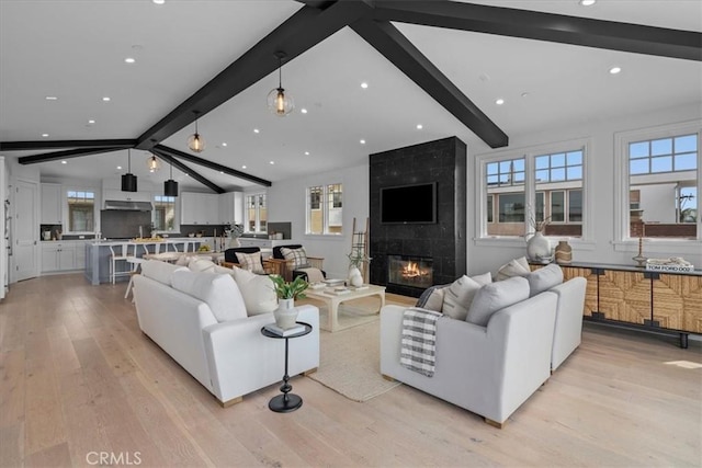 living area with vaulted ceiling with beams, a healthy amount of sunlight, a premium fireplace, and light wood-style floors