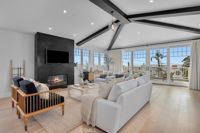 living room featuring vaulted ceiling with beams, light wood-type flooring, a healthy amount of sunlight, and a fireplace