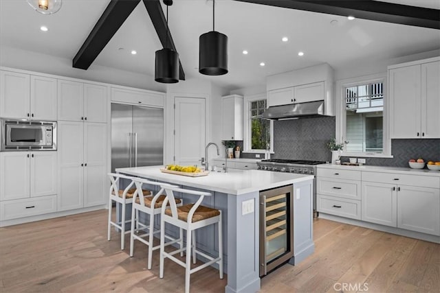 kitchen featuring beverage cooler, under cabinet range hood, light wood finished floors, and built in appliances