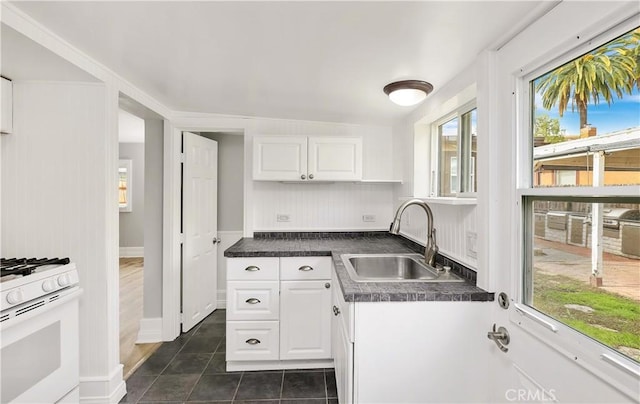 kitchen with white cabinets, dark countertops, a sink, dark tile patterned floors, and gas range gas stove