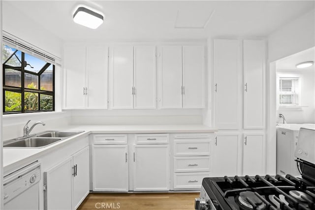 kitchen featuring stainless steel gas range, white dishwasher, a sink, and white cabinetry