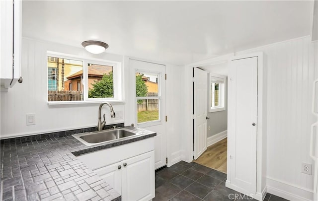 kitchen featuring dark countertops, white cabinetry, a sink, and baseboards