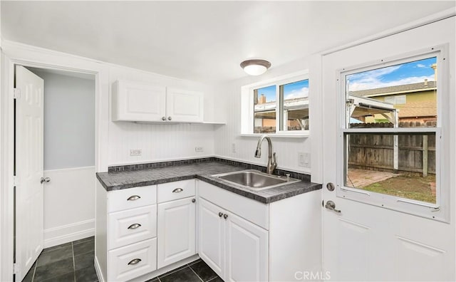 kitchen featuring dark tile patterned flooring, dark countertops, a sink, and white cabinets