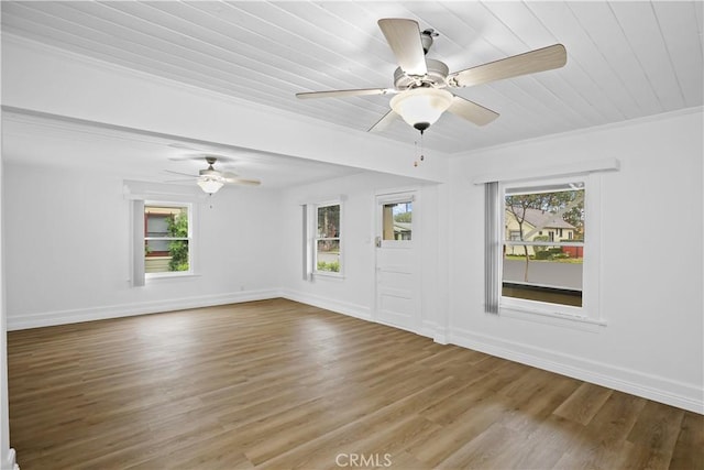 empty room featuring a ceiling fan, plenty of natural light, baseboards, and wood finished floors