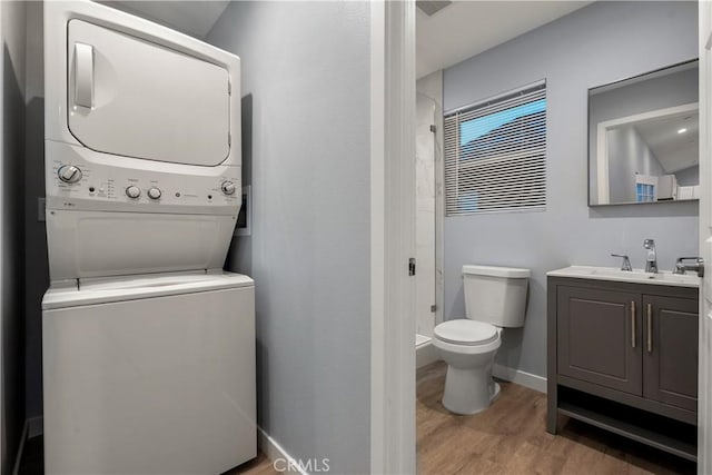 clothes washing area featuring stacked washer and dryer, light wood-style floors, a sink, laundry area, and baseboards