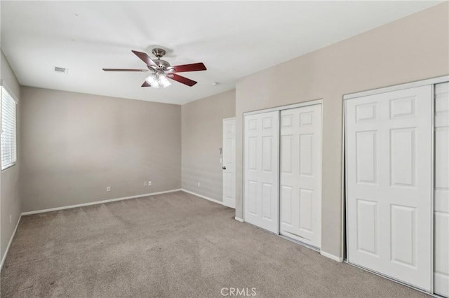 unfurnished bedroom with visible vents, baseboards, ceiling fan, carpet flooring, and two closets