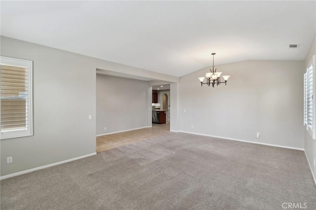 carpeted empty room featuring lofted ceiling, baseboards, visible vents, and a chandelier