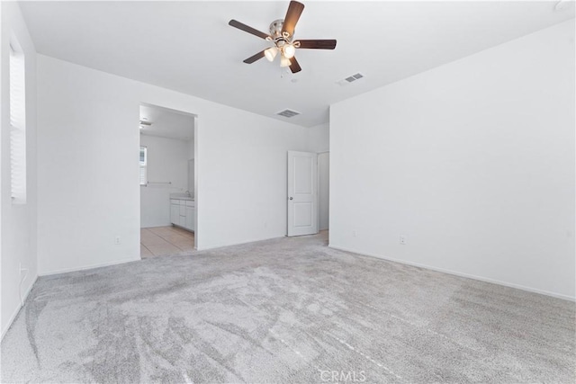 unfurnished bedroom featuring visible vents, ensuite bathroom, a ceiling fan, and light colored carpet