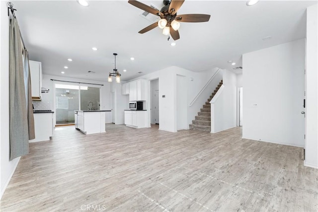 unfurnished living room featuring light wood finished floors, recessed lighting, visible vents, a ceiling fan, and stairs