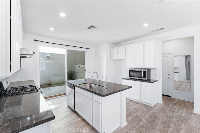 kitchen featuring visible vents, appliances with stainless steel finishes, light wood-style floors, a sink, and dark stone countertops