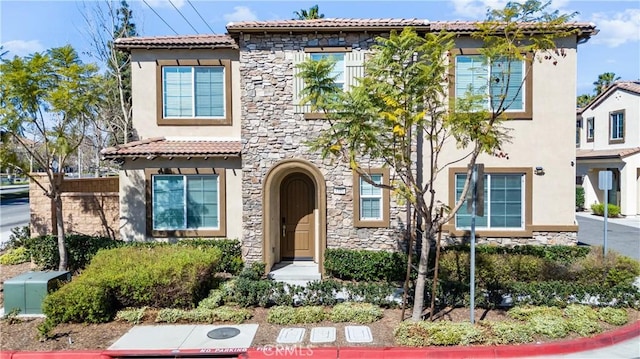 mediterranean / spanish-style house with stone siding, a tile roof, and stucco siding