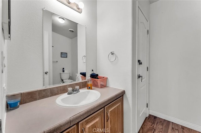 bathroom with toilet, baseboards, wood finished floors, and vanity