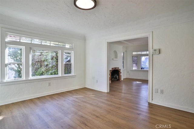 unfurnished living room featuring a textured ceiling, a fireplace, baseboards, and wood finished floors