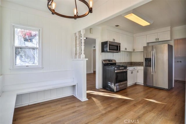 kitchen with appliances with stainless steel finishes, white cabinets, and wood finished floors