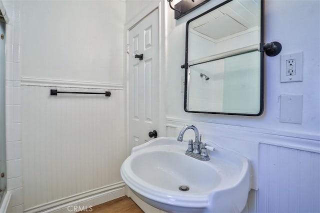 full bath featuring a wainscoted wall, a shower, a sink, and wood finished floors