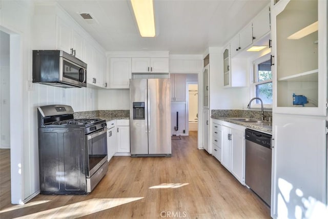 kitchen featuring stainless steel appliances, dark stone countertops, a sink, and white cabinets